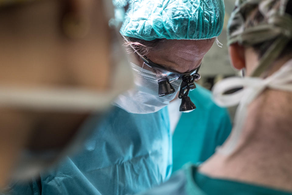 Three surgeons in an operating room, one focusing closely on the surgery with magnifying loupes