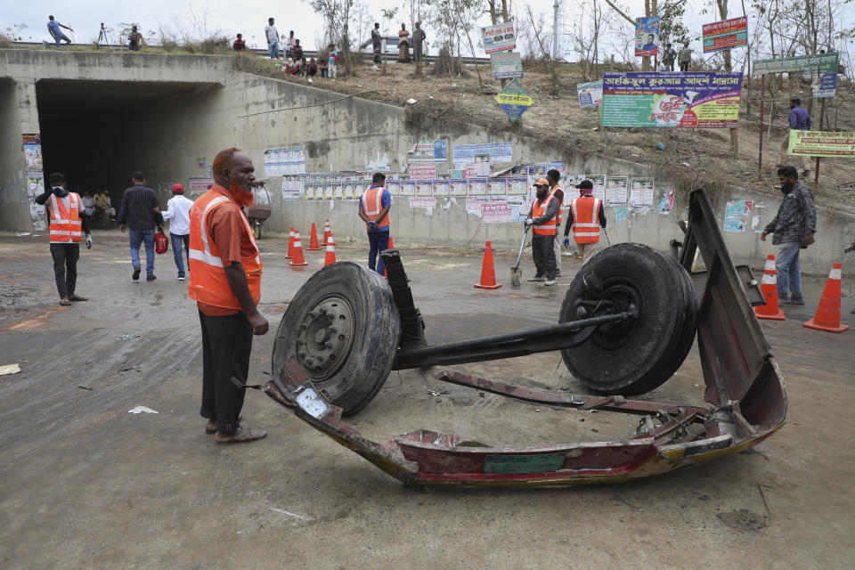 Volunteers stand near the wreckage of a bus that fell into a roadside ditch in Shibchar area in Madaripur district, Bangladesh, Sunday, March 19, 2023. More than a dozen people were killed and more were injured in the accident. (AP Photo/Jibon Ahmed)