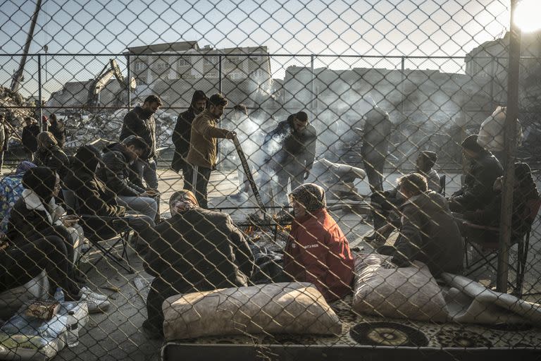 Supervivientes del terremoto se reúnen alrededor de una hoguera cerca de edificios derrumbados en Antakya