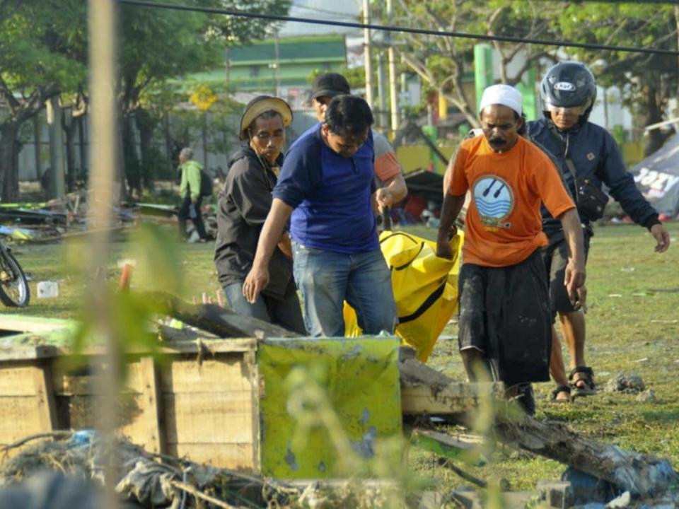 Residents carry a quake victim through Palu (AP)