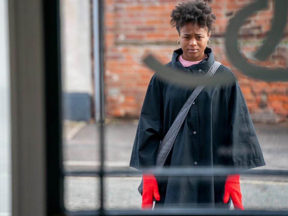 Bukky Bakray standing outside a window in a scene from the strays