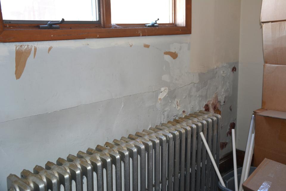 Behind the radiators on the second floor show damaged walls and peeling paint.
