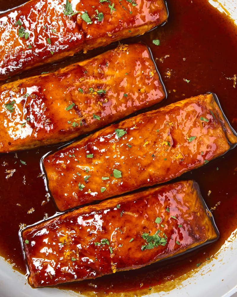overhead shot of four pieces of harissa orange glazed salmon in a pan, topped with herbs.