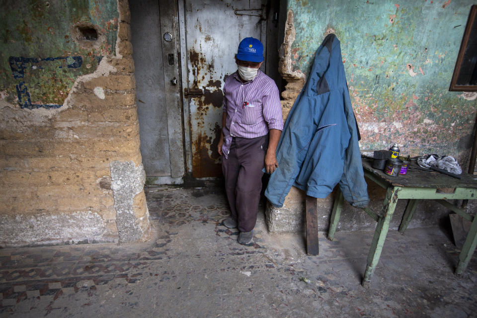 El vendedor de helados Juan Velásquez, de 58 años, pasa frente a una cámara frigorífica en el interior de la casa en desuso utilizada para almacenar los carros del vendedor y donde viven algunos de ellos durante la pandemia de COVID-19 en la Ciudad de Guatemala, el martes 26 de mayo de 2020. (AP Foto/Moises Castillo)