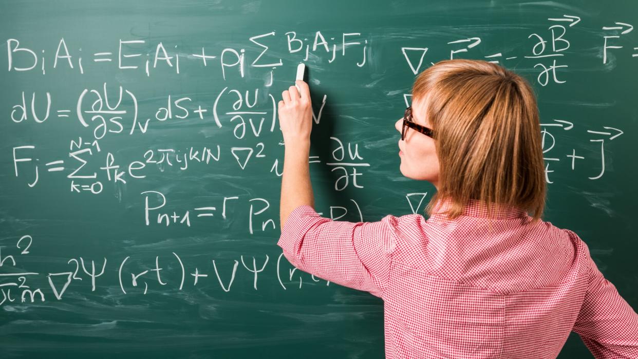 "Close-up on woman in glasses standing against green chalkboard.