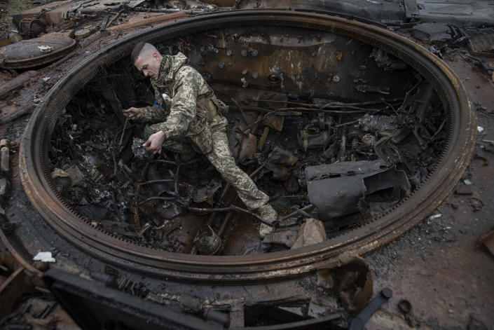 A Ukrainian soldier inspects a burned Russian tank.