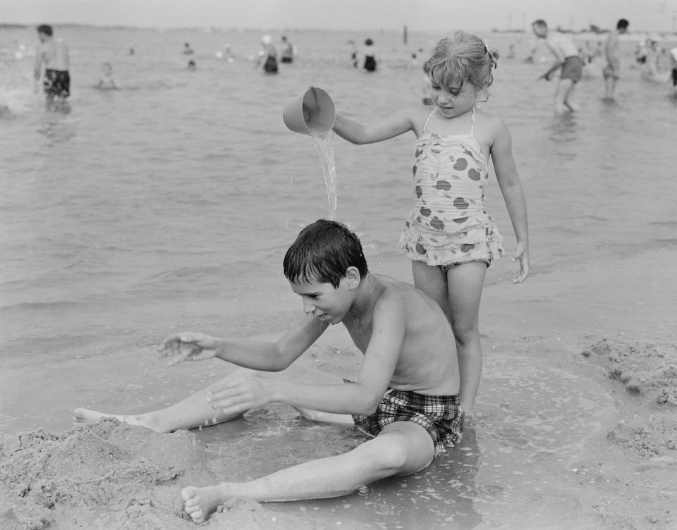 sister pouring water from bucket at his brother on beach