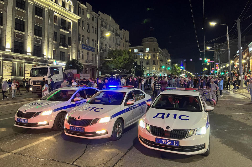 Three Russian police cars appear to be parked side-by-side in the middle of a large road near onlookers.