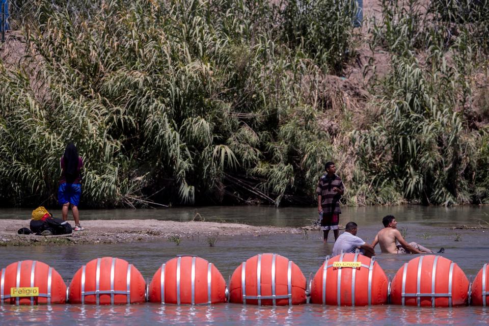 Migrants rest near Buoys on the U.S. side of the Rio Grande in Eagle Pass, Texas on July 20. The buoys were installed on orders by Texas Governor Greg Abbot to prevent migrants from reaching the north embankment of the Rio Grande on the international boundary between Mexico and the U.S.