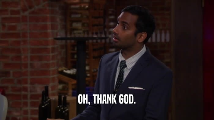 Aziz Ansari in a suit and tie with a pocket square in a brick-walled room saying, "Oh, thank God."