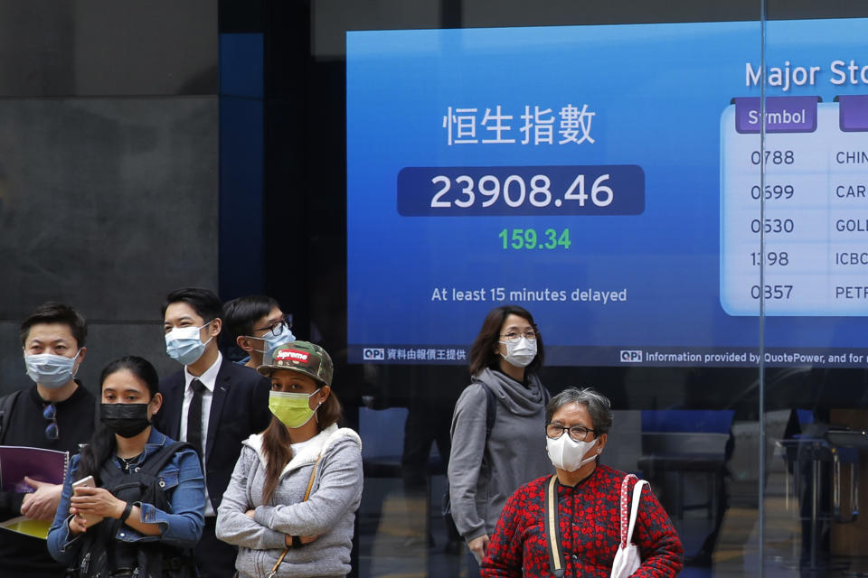 People wearing face masks stand in front of an electronic board showing Hong Kong share index outside a local bank in Hong Kong, Tuesday, April 7, 2020. Asian shares are rising, echoing the rally on Wall Street fueled by signs of hope that the coronavirus pandemic could be slowing. (AP Photo/Kin Cheung)