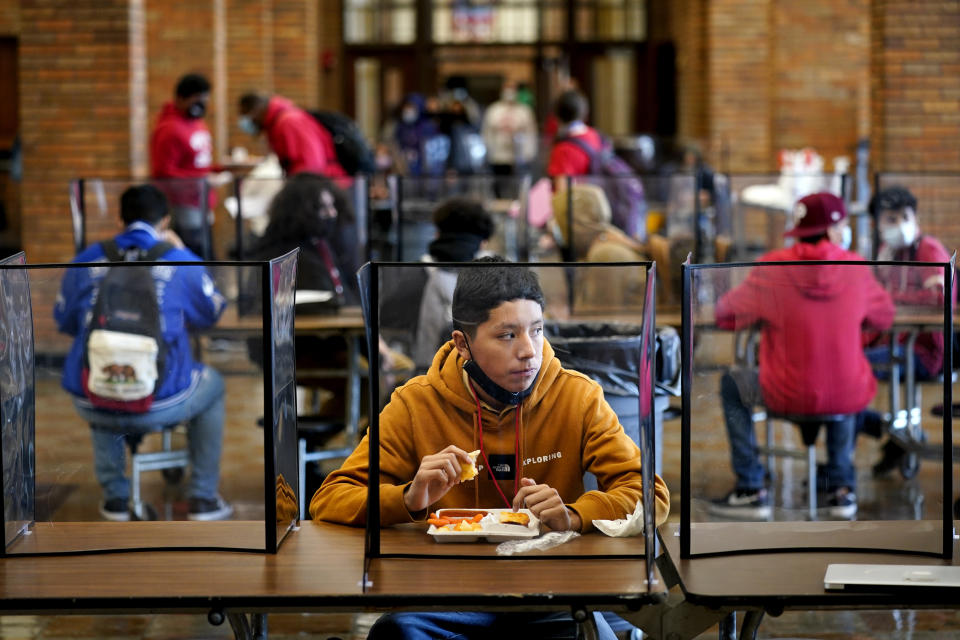 FILE - In this March 31, 2021, file photo, freshman Hugo Bautista eats lunch separated from classmates by plastic dividers at Wyandotte County High School in Kansas City, Kan., on the first day of in-person learning. With a massive infusion of federal aid coming their way, schools across the U.S. are weighing how to use the windfall to ease the harm of the pandemic — and to tackle problems that existed long before the coronavirus. (AP Photo/Charlie Riedel, File)