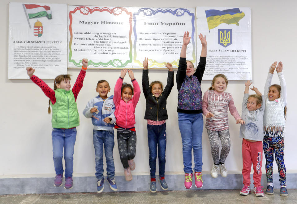 In this Friday, Oct. 19, 2018 photograph, children jump in front of posters with the Hungarian and Ukrainian anthems and national symbols at the Velyka Dobron High School in Velyka Dobron, Ukraine. A new education law that could practically eliminate the use of Hungarian and other minority languages in schools after the 4th grade is just one of several issues threatening this community of 120,000 people. Many are worried that even as Ukraine strives to bring its laws and practices closer to European Union standards, its policies for minorities seem to be heading in a far more restrictive direction. (AP Photo/Laszlo Balogh)