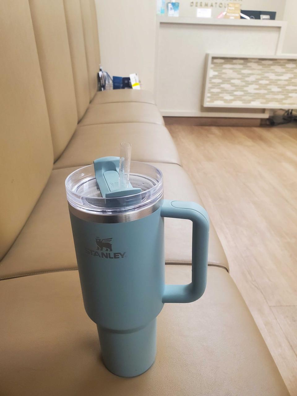 A teal Stanley cup rests on a brown leather seat.