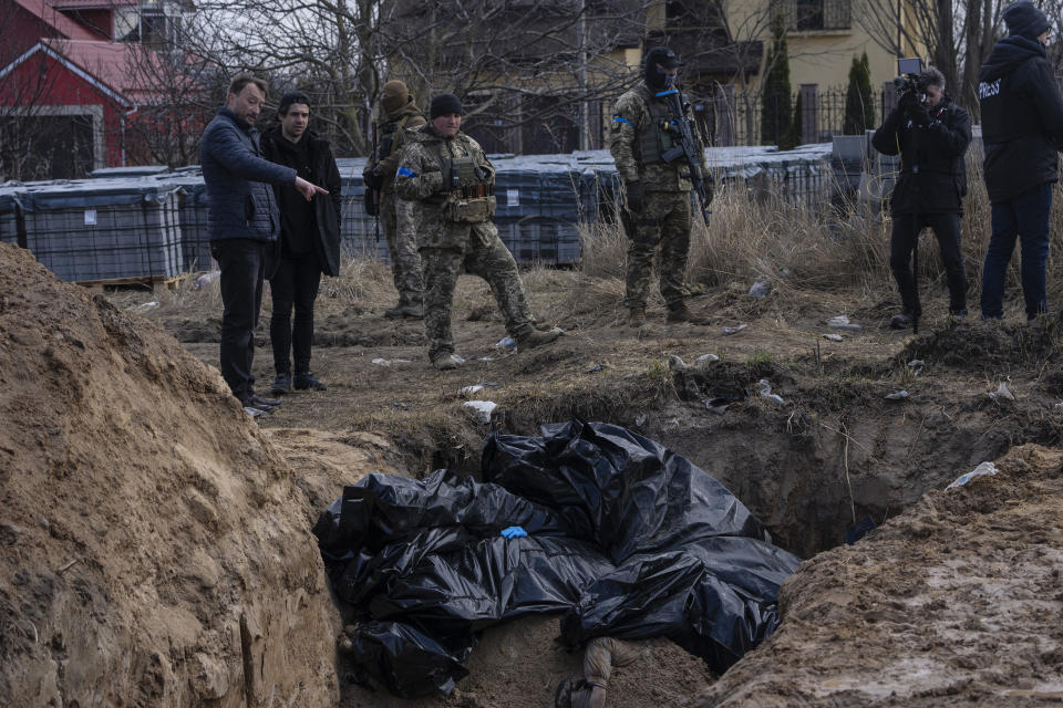 FILE - People stand next to a mass grave in Bucha, on the outskirts of Kyiv, Ukraine, April 4, 2022. The Kremlin and Russian state media are aggressively pushing a baseless conspiracy theory blaming the United States for damage to natural gas pipelines in the Baltic Sea in what analysts said Friday, Sept. 30, 2022 is another effort to split the U.S. and its European allies. (AP Photo/Rodrigo Abd, File)