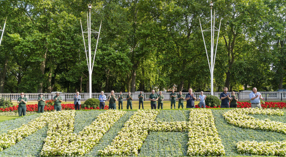 Royal Parks staff applaud the NHS's 72 birthday behind one of two specially created 12 x 5 metre flowerbeds in front of Buckingham Palace in the Memorial Gardens in St James's Park. The letters are made up of 1,500 Begonia semperflorens 'Heaven White' plants in each bed, while the background is 21,000 plants of Echeveria imbricate, Senecio serpens and Sedum pachyclados.