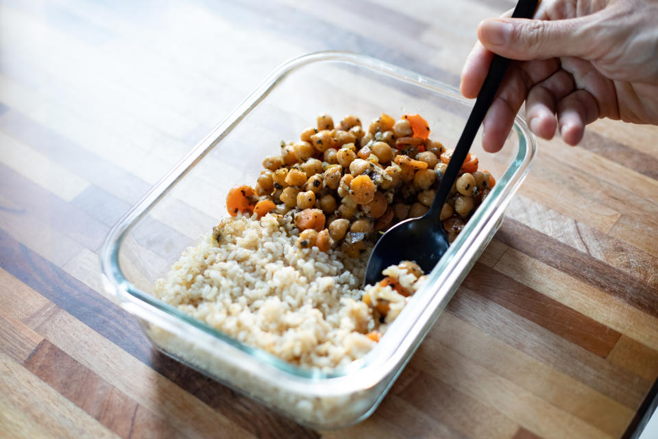 Meal prep concept with chickpeas, carrots, and rice in a glass container being eaten with a fork