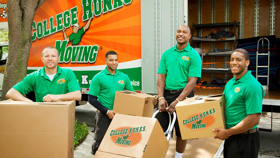 A team of College Hunks movers stand in front of a moving truck