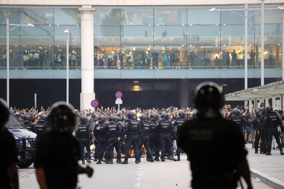 A line of riot police stands in front of protestors outside El Prat airport in Barcelona, Spain, Monday, Oct. 14, 2019. Riot police have charged at protesters outside Barcelona's airport after the Supreme Court sentenced 12 prominent Catalan separatists to lengthy prison terms for their roles in a 2017 push for the wealthy Spanish region's independence. (AP Photo/Emilio Morenatti)