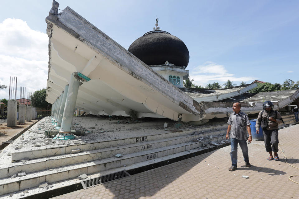 People walk near a collapsed mosque following an earthquake in Meureudu