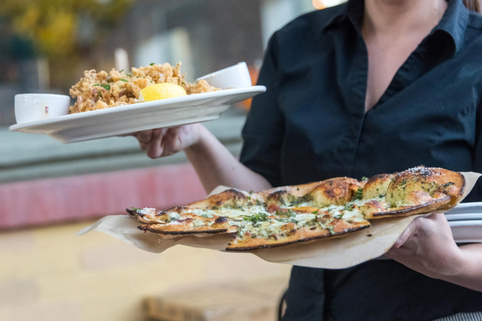 A server carries a plate of fried food and a plate with slices of pizza