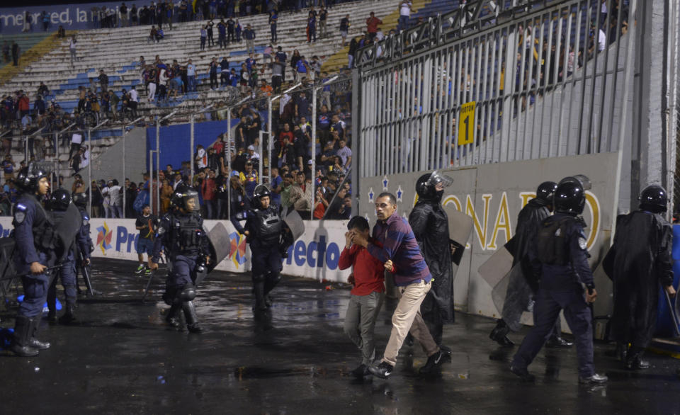 A man and youth walk with their eyes shut due to tear gas fired by police trying to break up a deadly fight between fans before the start of a game between Motagua and Olimpia, inside the national stadium in Tegucigalpa, Honduras, late Saturday, Aug. 17, 2019. The fight between fans of rival soccer teams outside the stadium left three people dead and led to the suspension of the game. (Victor Colindres/La Tribunal via AP)