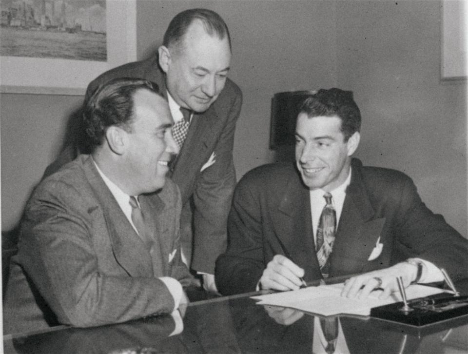 Joe DiMaggio, right, the New York Yankees great center fielder, smiles broadly as he signs his 1949 contract in the Yankees’ office in New York on Feb. 7, 1949. At left is Dan Topping, one of the owners and president of the Yankees. George Weiss, the club’s general manager, stands between them. The contract is for one year and is worth $100,000. (AP Photo/Anthony Camerano)