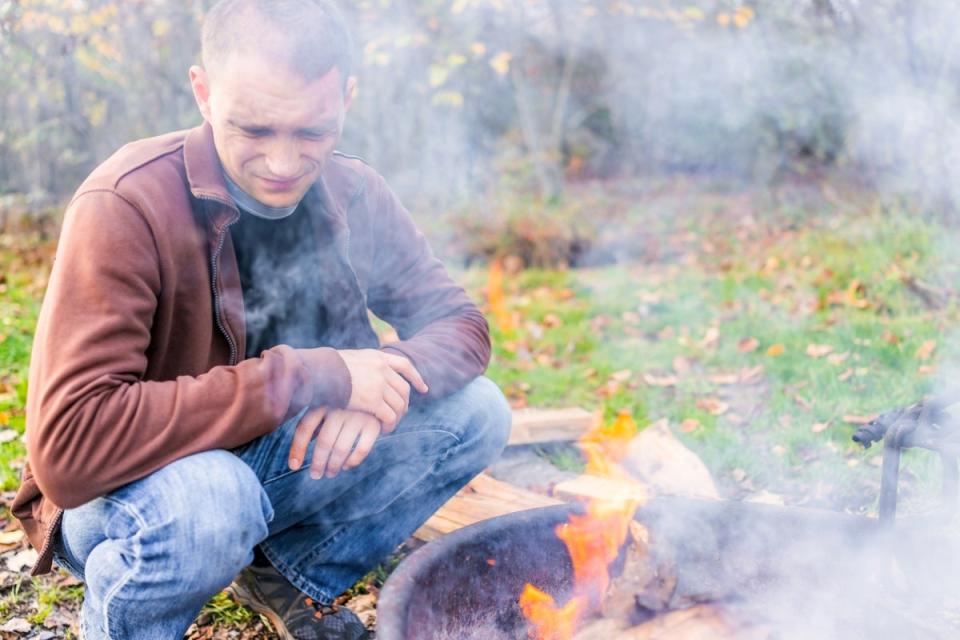 Smoke from fire pit blows in a man's face