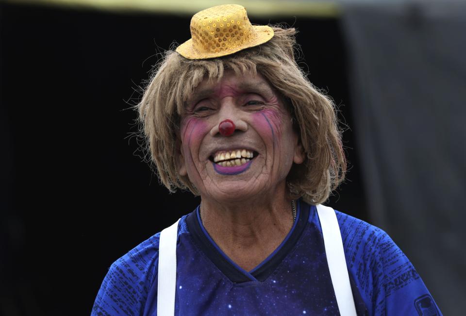 Circus clown Santos Chiroque, whose performance name is "Piojito," or Little Tick, laughs at his grandchild's comment that he looks like a woman, as he shows off his clown costume outside his home on the outskirts of Lima, Peru, Monday, Aug. 10, 2020. Chiroque's family used to run their own small circus, but since March when the lockdown to curb COVID-19 closed their business, and the requirement for people over 60 to self-quarantine kept the 74-year-old at home, they started selling circus food like caramelized apples to survive. (AP Photo/Martin Mejia)