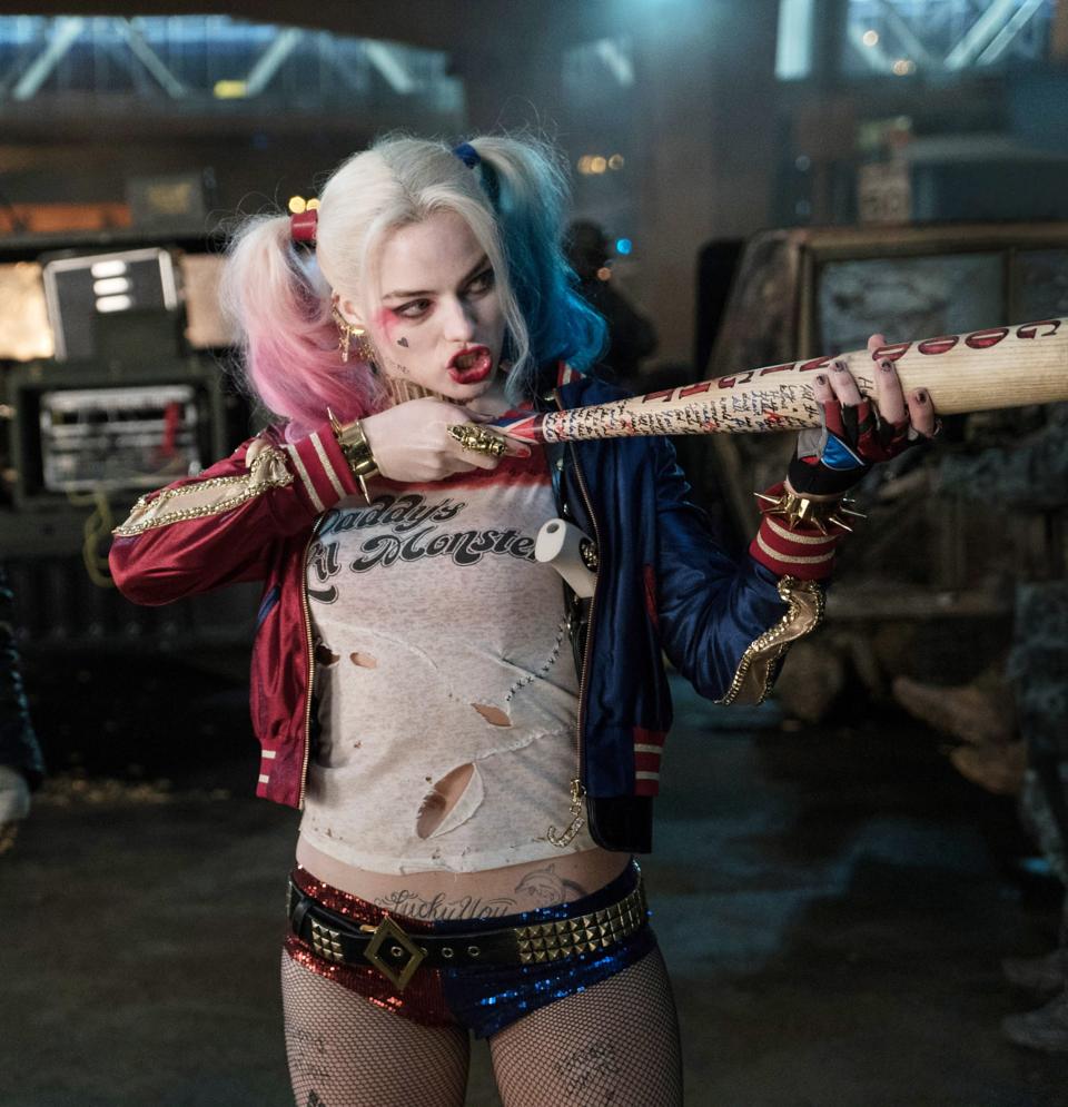 Harley Quinn in a torn shirt, shorts, and jacket holds a bat