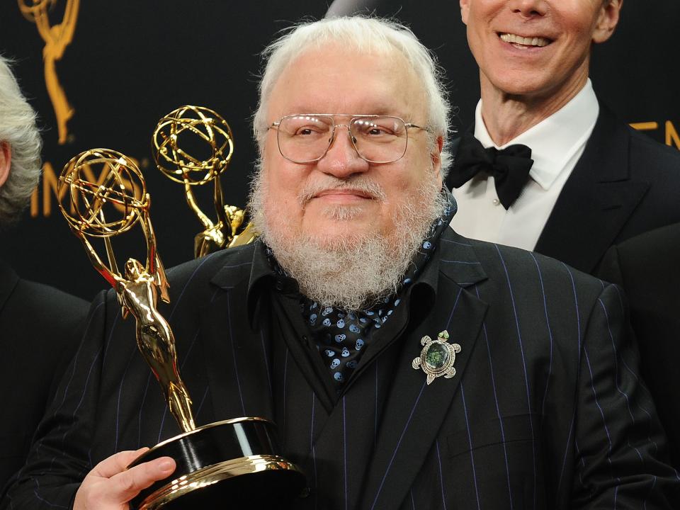 george r.r. martin in a pinstripe suit, holding an emmy award and smiling