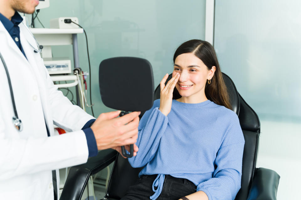 A woman smiles as she looks in the mirror during a post-op doctor's visit