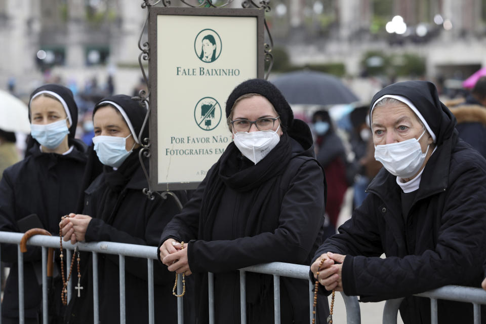 A group of nuns wearing face masks hold rosaries while waiting for the start of the religious ceremonies at the Catholic shrine in Fatima, Portugal, Thursday, May 13, 2021. In view of the coronavirus pandemic, the shrine has limited to 7,500 the number of pilgrims that can be present during this year's May 12 and 13 celebrations usually attended by hundreds of thousands. The sign reads " Speak low" and " Please don't take group photos". (AP Photo/Ana Brigida)