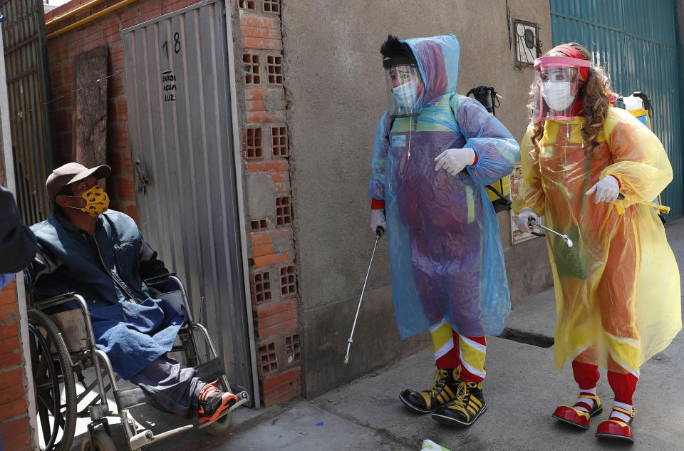 Image: Clowns Perlita and Tapetito, wearing protective gear amid the new coronavirus pandemic, speak with resident Enrique Zeballos as they arrive to disinfect his home free of charge, in El Alto, Bolivia (Juan Karita / AP)