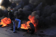 A protester kicks a burning tire to block a highway that links to the Beirut's international airport, in Beirut, Lebanon, Tuesday, March 2, 2021. Scattered protests broke out in different parts of Lebanon Tuesday after the Lebanese pound hit a record low against the dollar on the black market, a sign of the country's multiple crises deepening with no prospects for a new Cabinet in the near future. (AP Photo/Hussein Malla)