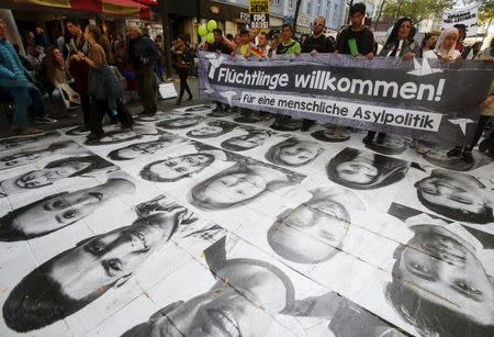 Protesters march over portraits of refugees, laid out as an arts project, during a demonstration in support of refugees in Vienna, Austria, October 3, 2015. REUTERS/Heinz-Peter Bader