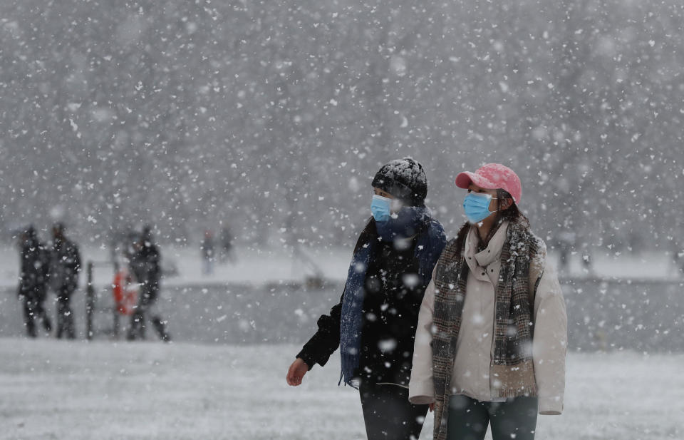 Pedestrians wearing face masks against the coronavirus pandemic walk in Kensington Gardens as snow falls in London, Sunday, Jan. 24, 2021. (AP Photo/Alastair Grant)