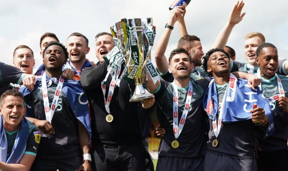 Plymouth Argyle manager, Steven Schumacher, celebrates by lifting the trophy with his players after winning the League One title