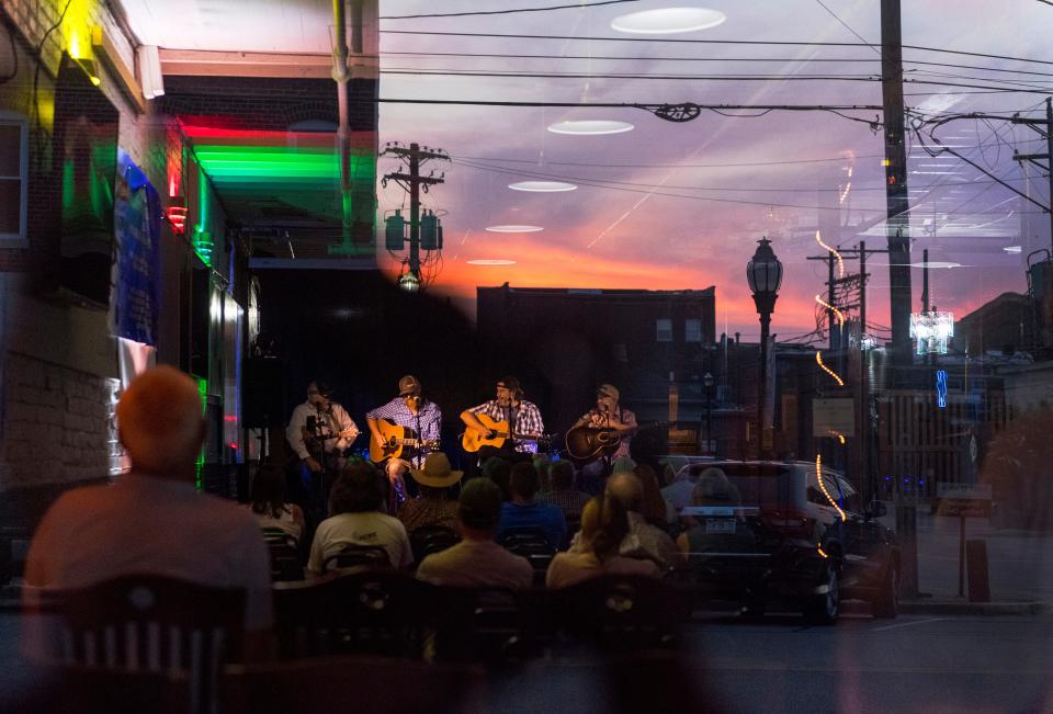 Downtown Henderson is reflected off a window as Rusty Tabor, second from left, performs during the 2021 Sandy Lee Watkins Songwriters Festival at the Elks Lodge in Henderson, Ky., Wednesday evening, July 28, 2021. 