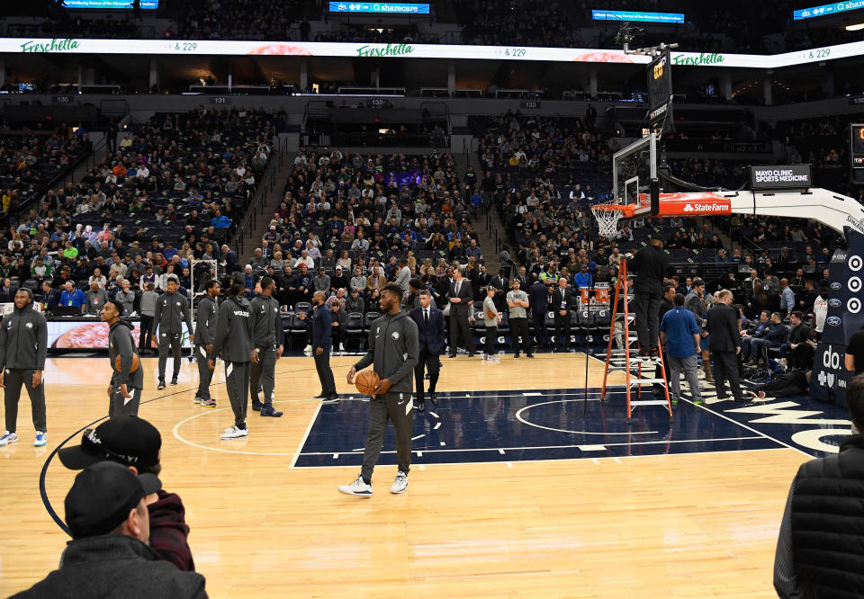 The Minnesota Timberwolves look on as workers inspect a hoop before the game against the Milwaukee Bucks.