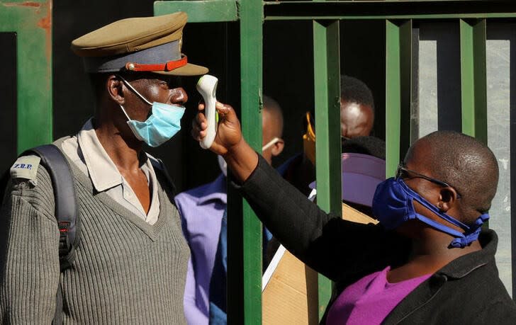 FILE PHOTO: A person checks a policeman's temperature during a nationwide lockdown to help curb the spread of the coronavirus disease (COVID-19) in Harare