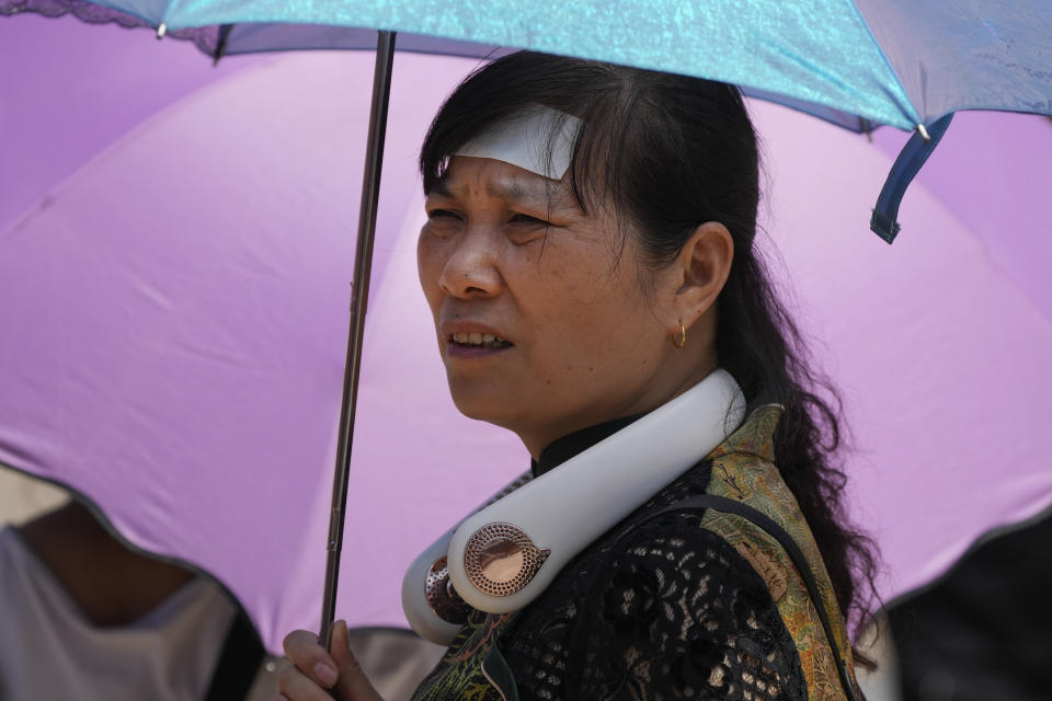 A woman wearing an electric fan, putting a cooling pad on her forehead and carrying an umbrella visits the Forbidden City on a sweltering day in Beijing, Friday, July 7, 2023. Earth's average temperature set a new unofficial record high on Thursday, the third such milestone in a week that already rated as the hottest on record. (AP Photo/Andy Wong)
