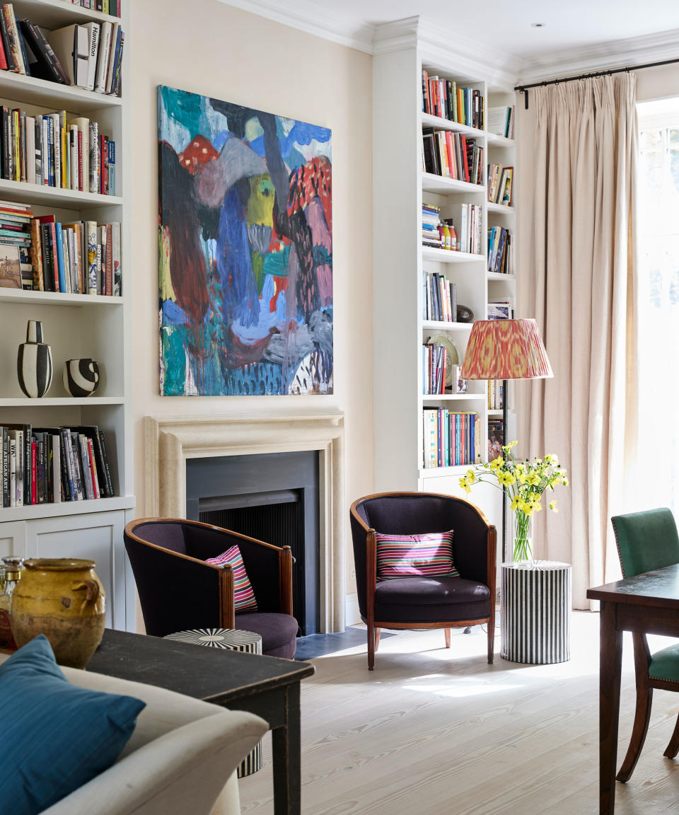 Large living room with tall bookshelves, fireplace, large artwork, cream walls and matching curtains