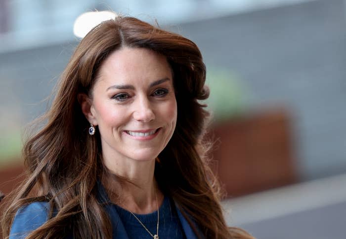 Kate Middleton, wearing a blazer and earrings, smiles while posing outdoors