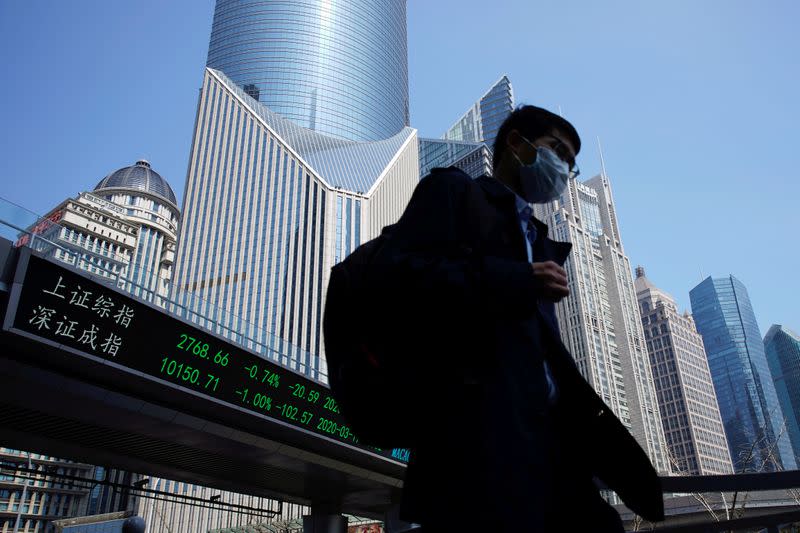 FILE PHOTO: Pedestrian wearing a face mask walks near an overpass with an electronic board showing stock information in Shanghai