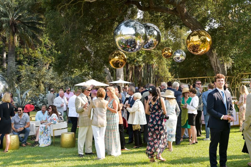 Guests mingle beneath reflective orbs on the shaded lawn.