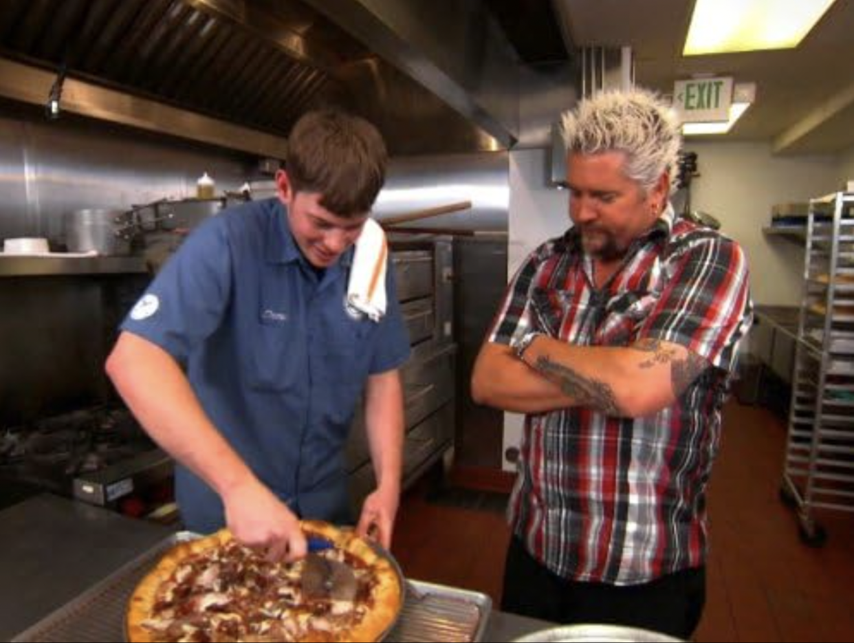 Guy in a kitchen cutting pizza