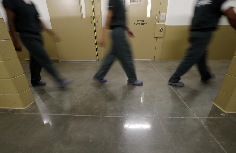 Inmates walk down a hallway at the Otay Mesa Detention Center Wednesday, Aug. 23, 2017, in San Diego. The facility was at the center of the first big novel coronavirus outbreak at a U.S. immigration detention center in April 2020. (AP Photo/Gregory Bull)