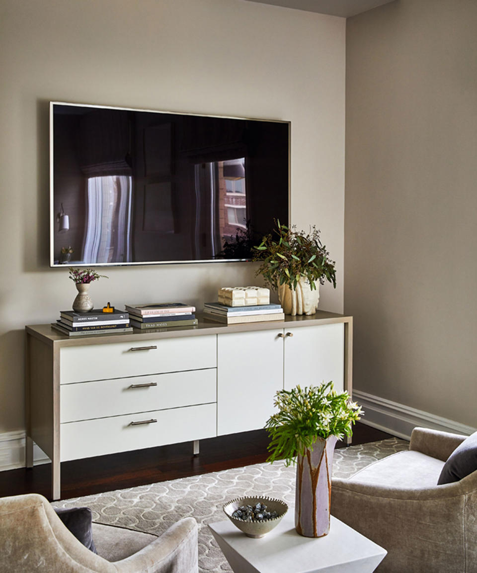 Modern living room with wall-mounted TV, wide and wood sideboard decorated with books, flowers and ornaments