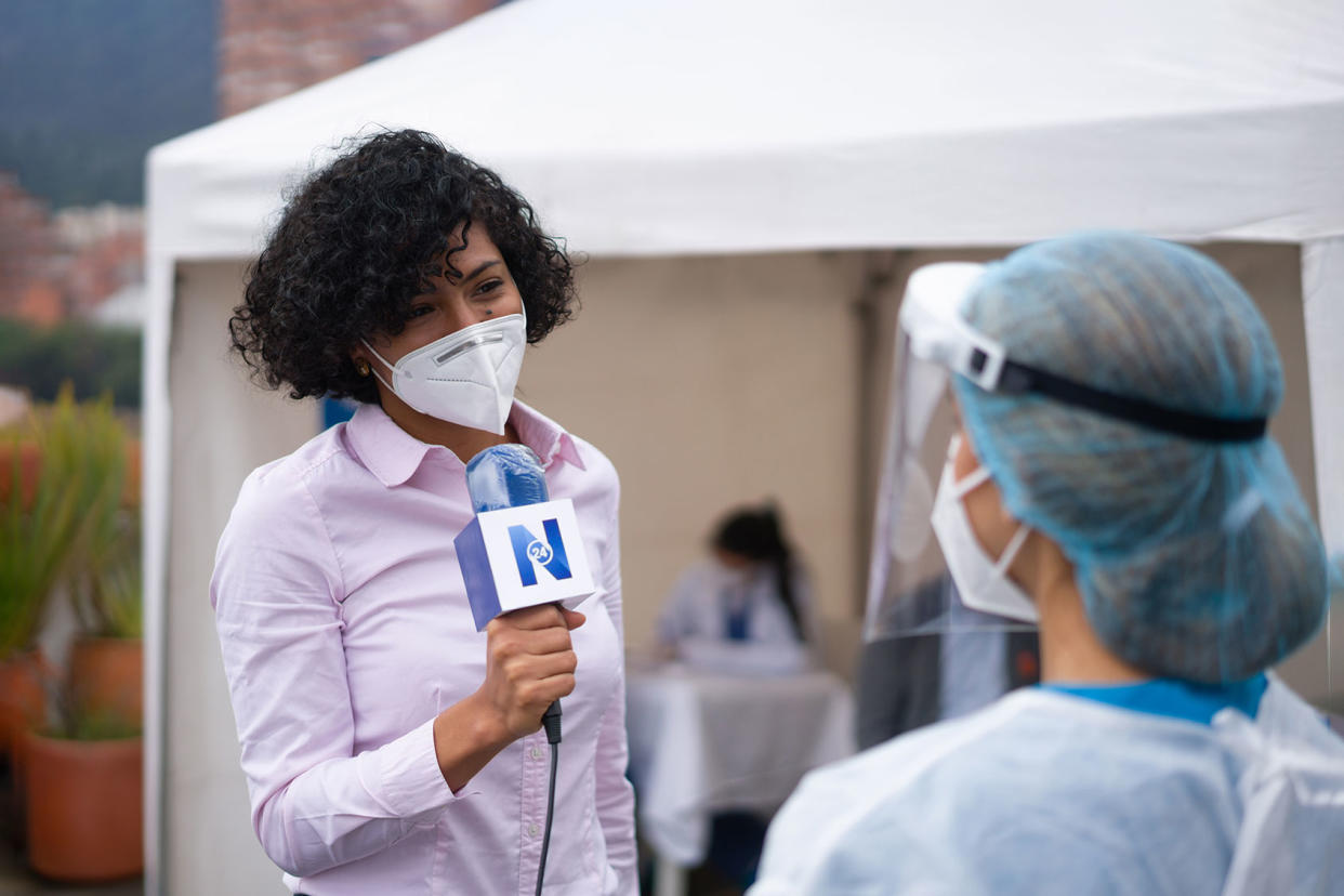 Journalist interviewing a healthcare worker working at a COVID-19 vaccination stand Getty Images/andresr